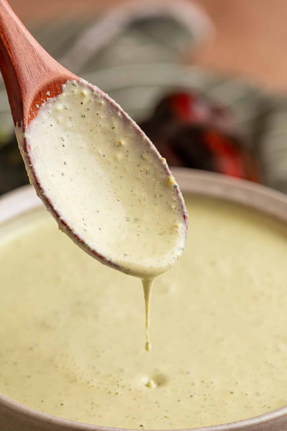 Close-up of creamy cilantro jalapeno dressing dripping from a wooden spoon over a bowl, showing the smooth, pourable texture.