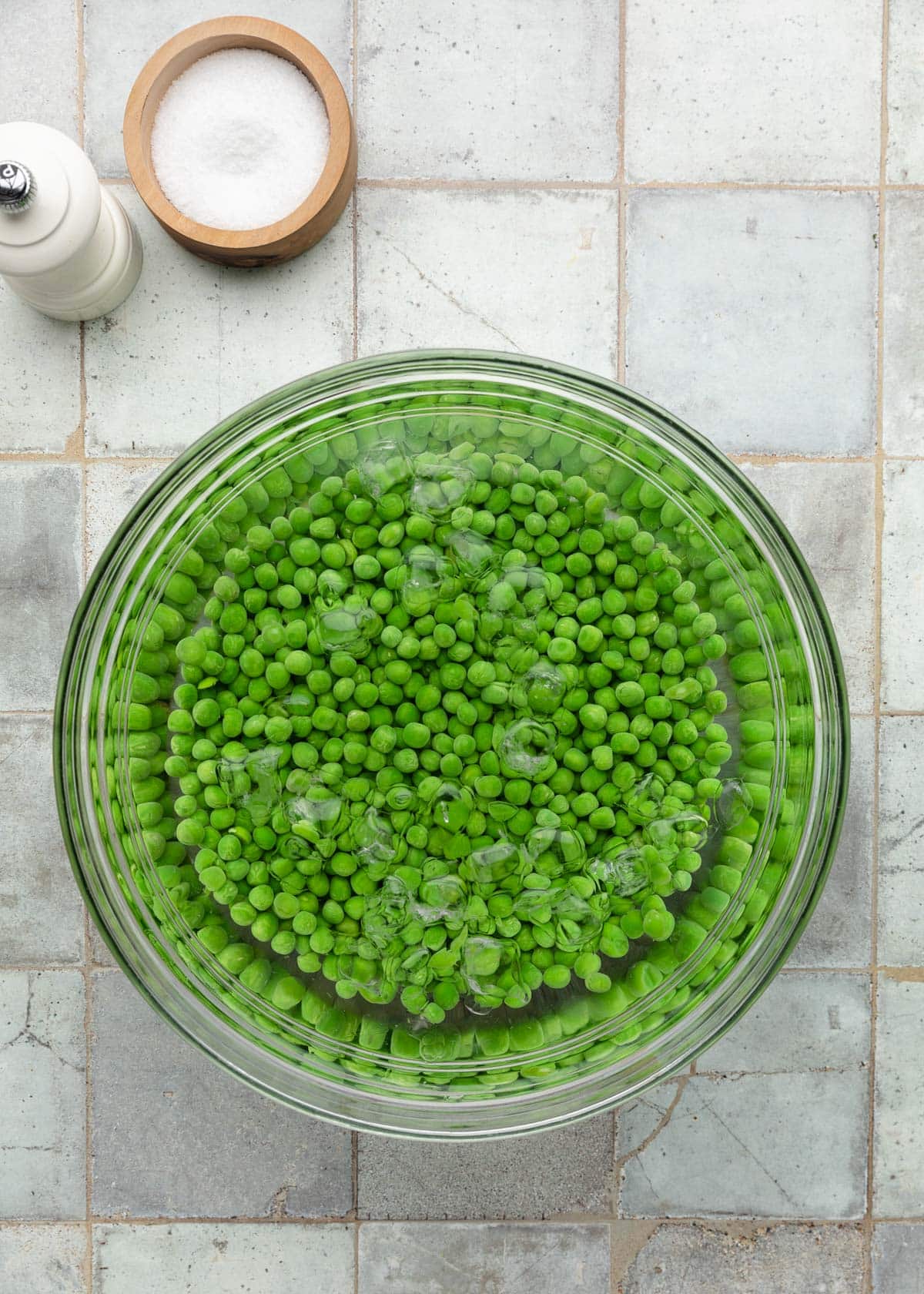 Top-down process photo of peas chilling in an ice water bath to stop the cooking and keep their bright green color.