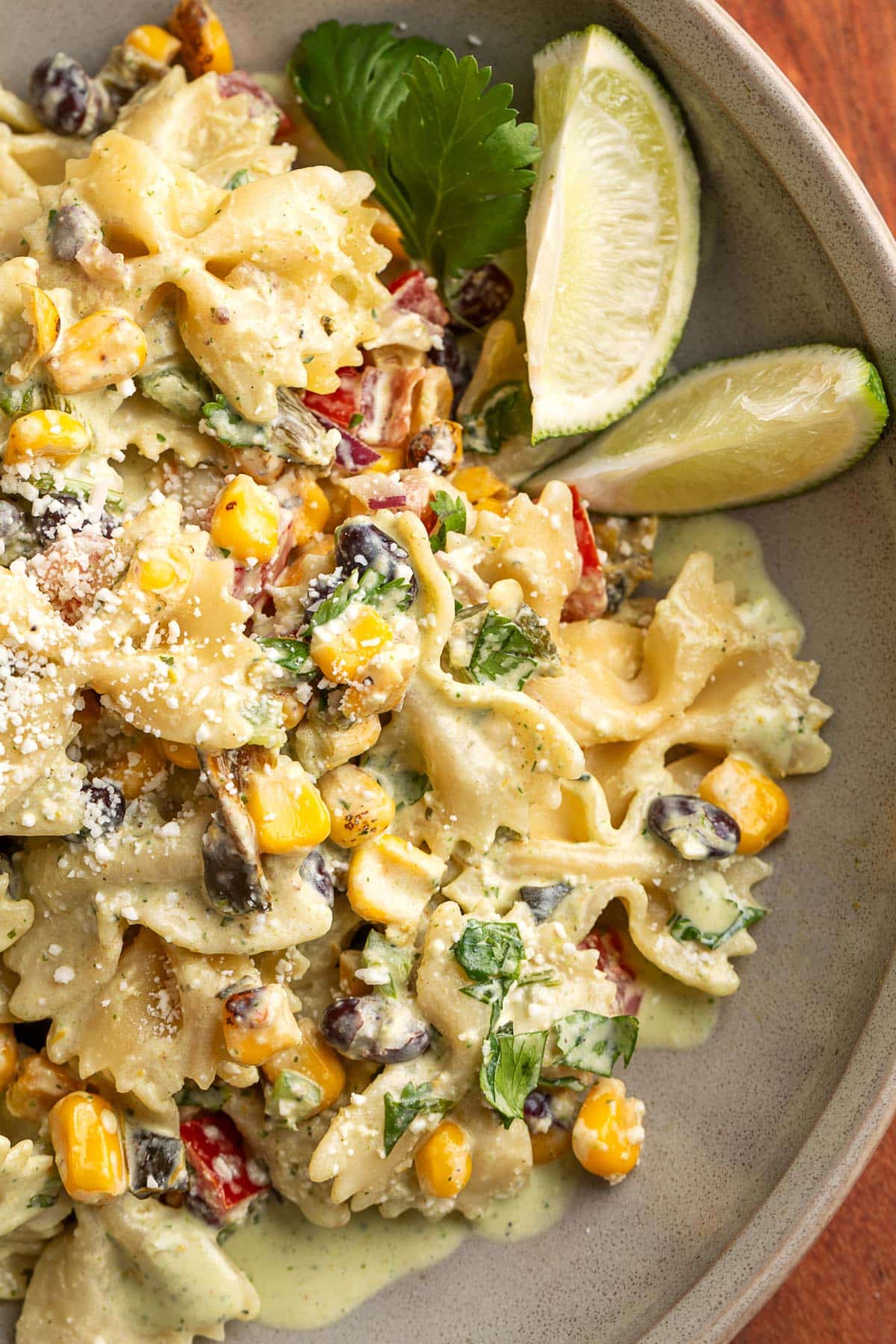 Bowl of Southwest pasta salad with farfalle pasta, black beans, roasted corn, cotija cheese, and creamy cilantro jalapeno dressing, garnished with lime wedges and fresh cilantro.