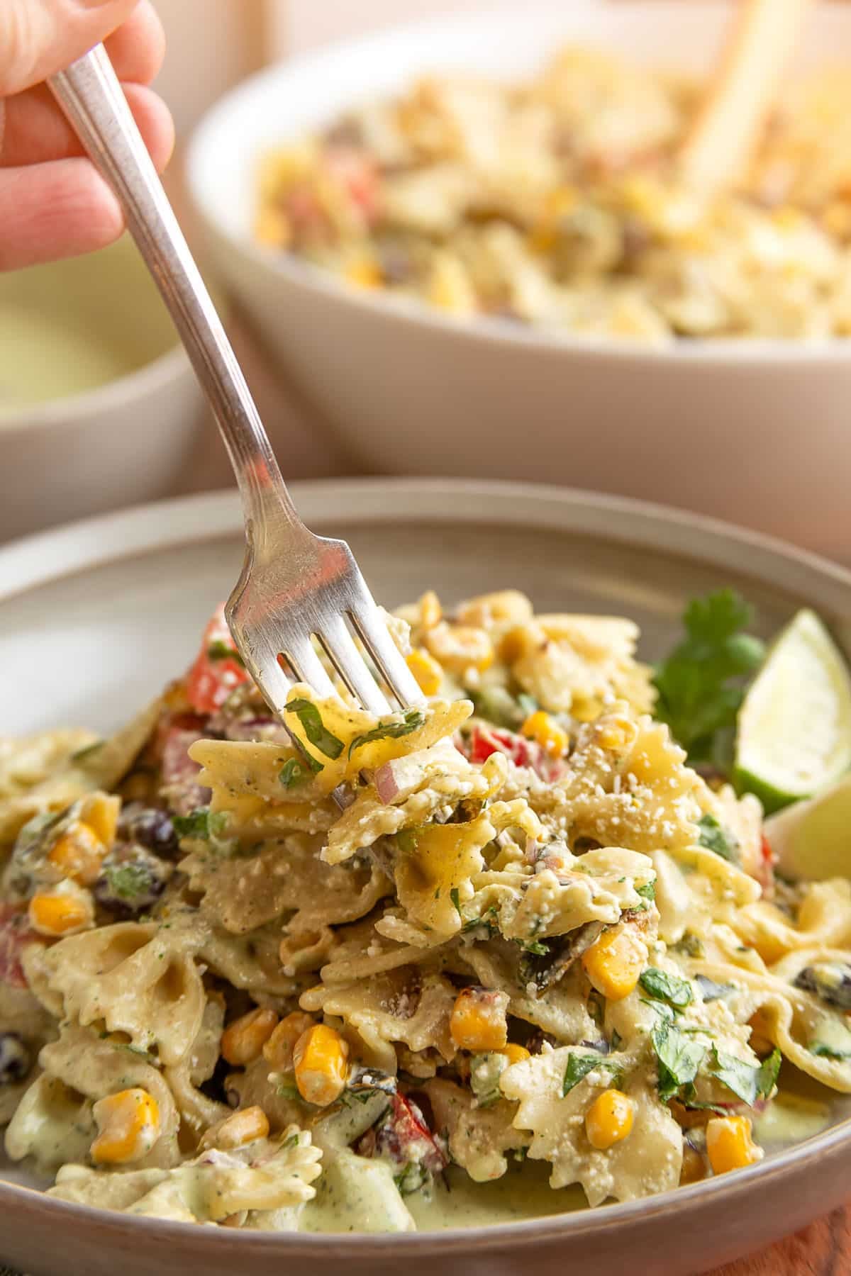 Fork lifting a bite of creamy Southwest pasta salad with farfalle pasta, black beans, roasted corn, poblano peppers, cotija cheese, and cilantro jalapeno dressing.