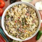 Large bowl of creamy Southwest pasta salad with farfalle pasta, black beans, roasted corn, tomatoes, poblano peppers, cotija cheese, and cilantro jalapeno dressing, surrounded by fresh ingredients.