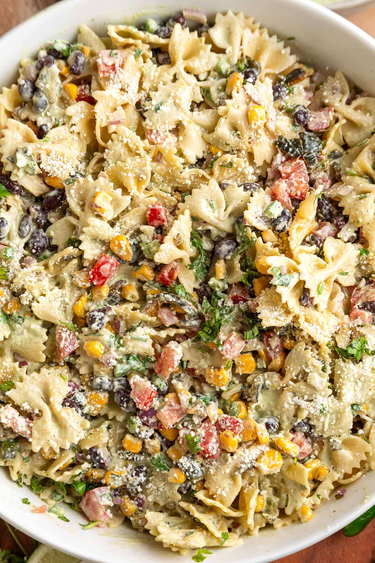 Overhead close-up of Southwest pasta salad made with farfalle pasta, black beans, fire roasted corn, tomatoes, poblano peppers, red onion, cilantro, cotija cheese, and creamy cilantro jalapeno dressing in a white serving bowl.