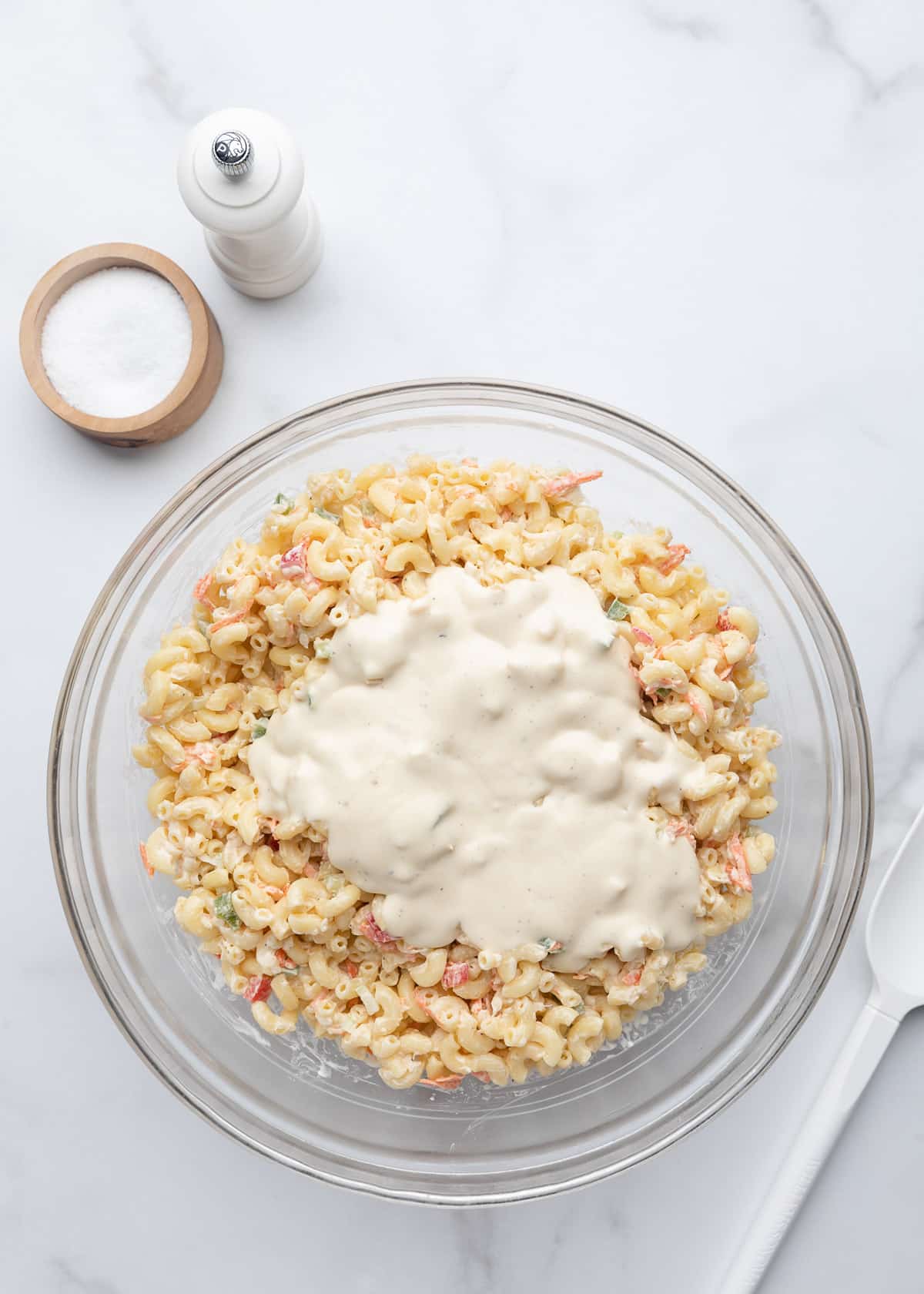Extra creamy macaroni salad with a fresh layer of dressing spread over the top, ready to stir in before serving.
