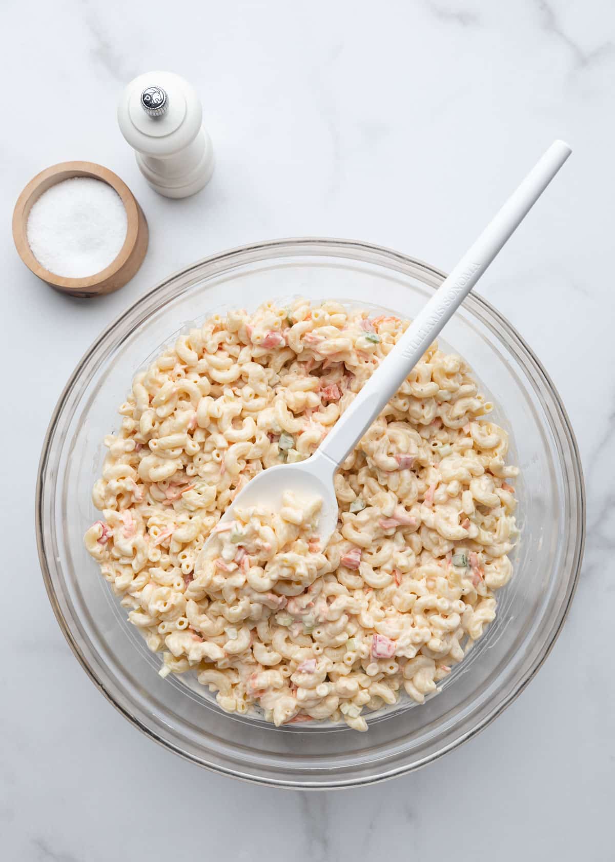 Macaroni salad fully mixed and coated in a creamy dressing, with grated carrots, celery, onion, and bell peppers distributed throughout the pasta.