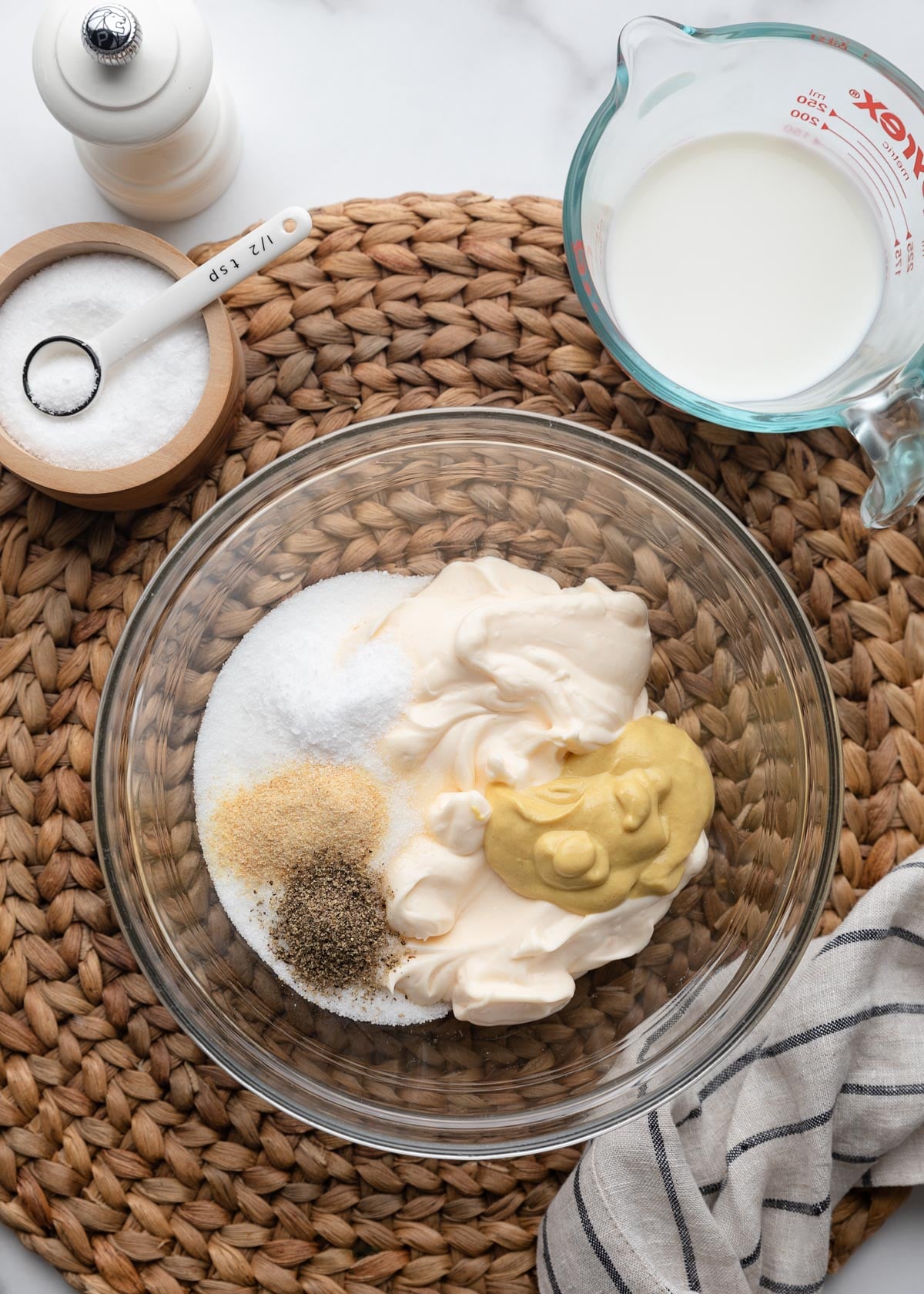 Mayonnaise, Dijon mustard, sugar, garlic powder, black pepper, and milk combined in a glass bowl to make the creamy dressing for classic macaroni salad.