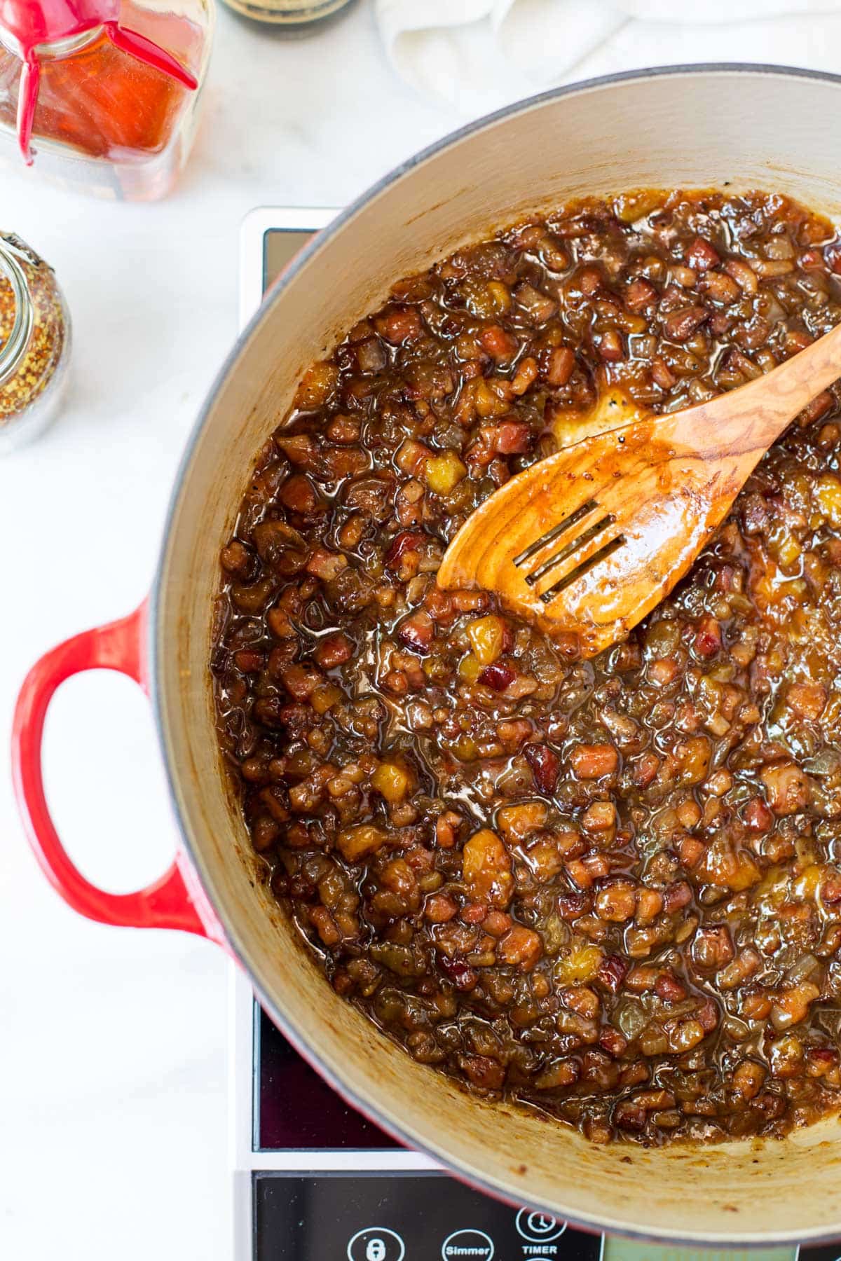 Peach bacon jam simmering in a Dutch oven until thick and glossy, with tender peaches, crispy bacon, caramelized onions, and a rich sweet-savory glaze. A wooden spoon stirs the finished jam as it cooks on the stovetop.