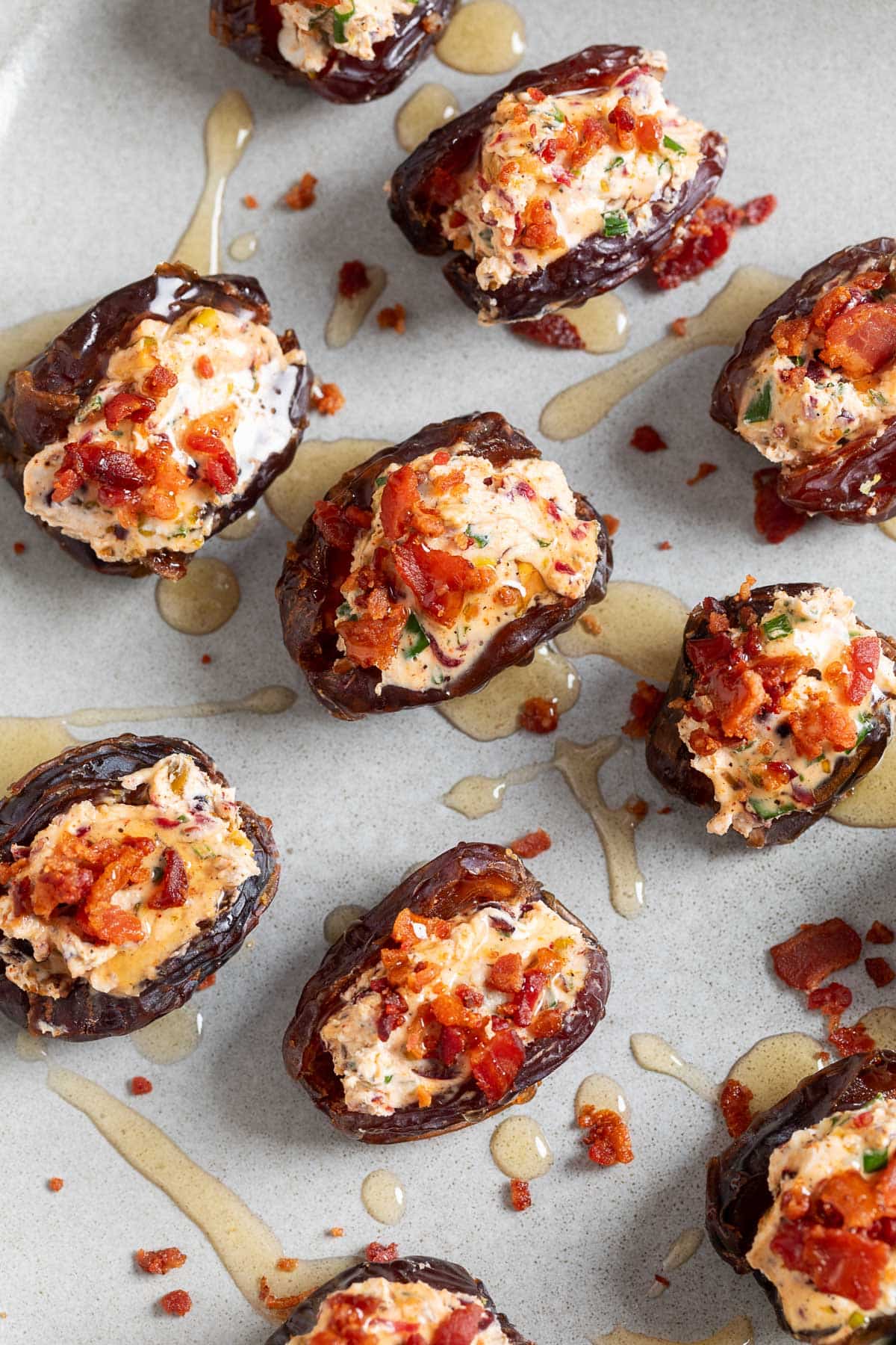 Dates stuffed with goat cheese mixed with pistachios, dried cranberries, herbs and seasonings, topped with crispy bacon crumbles and drizzled with hot honey, arranged on a serving platter.