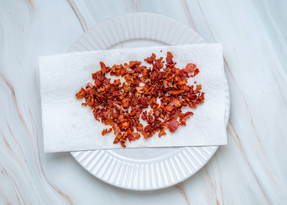 Crispy chopped bacon draining on a paper towel-lined plate after cooking.
