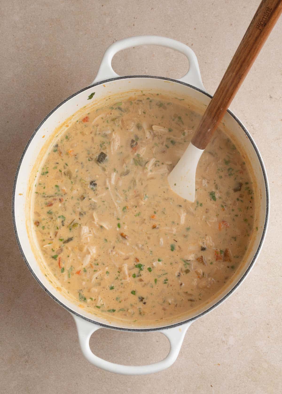 Creamy poblano white chicken chili with shredded chicken, diced roasted poblanos, cannellini beans, and flecks of fresh cilantro stirred throughout the thick, lightly orange-tinted broth in a white enameled Dutch oven.